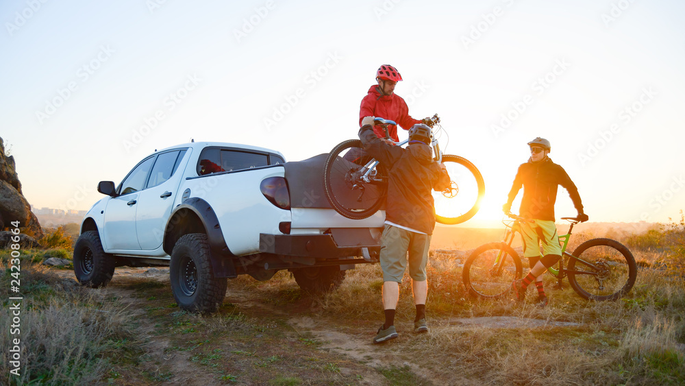 Friends Taking MTB Bikes off the Pickup Offroad Truck in Mountains at Sunset. Adventure and Travel Concept. - obrazy, fototapety, plakaty 