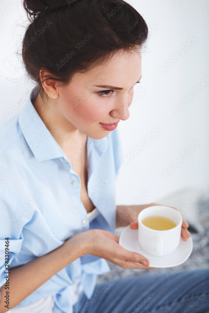 Young beautiful brunette woman, wearing jeans and blue shirt, drinking hot tea at home. Young beautiful brunette woman, wearing jeans and blue shirt, drinking hot tea at home.