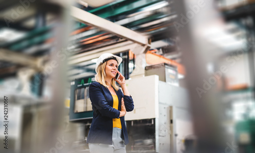 A portrait of an industrial woman engineer on the phone, standing in a factory.