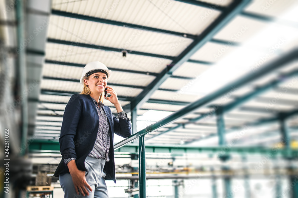 A portrait of an industrial woman with smartphone, standing in a factory. A portrait of an industrial woman with smartphone, standing in a factory.
