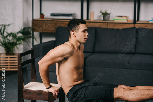 muscular mixed race man exercising on chair in living room