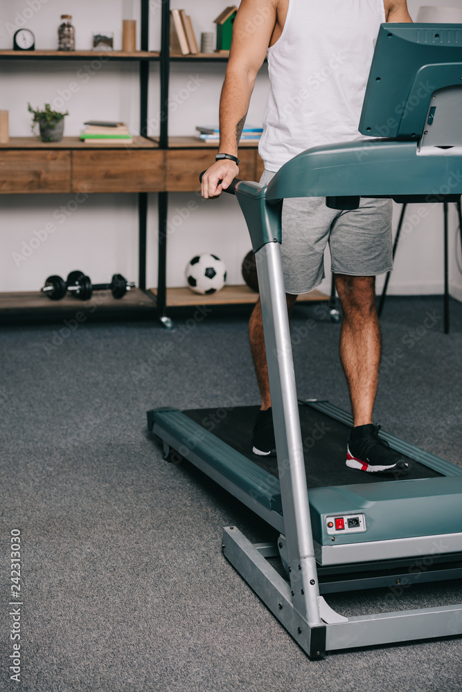 Fototapeta premium cropped view of man exercising on treadmill in living room