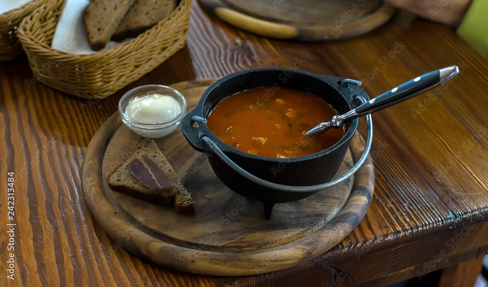 Russian soup, borsch, in a cast iron pot on the background of rye bread, on a wooden table in a stylish restaurant, in the old Russian style Russian soup, borsch, in a cast iron pot on the background of rye bread, on a wooden table in a stylish restaurant, in the old Russian style