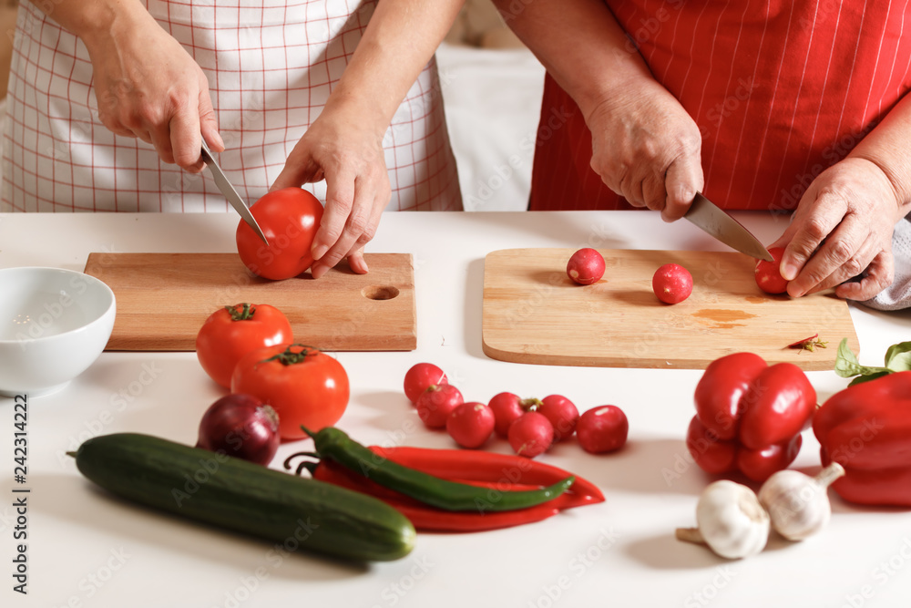 An adult daughter and an elderly mother are cooking together at home in the kitchen. Healthy fresh food. An adult daughter and an elderly mother are cooking together at home in the kitchen. Healthy fresh food.