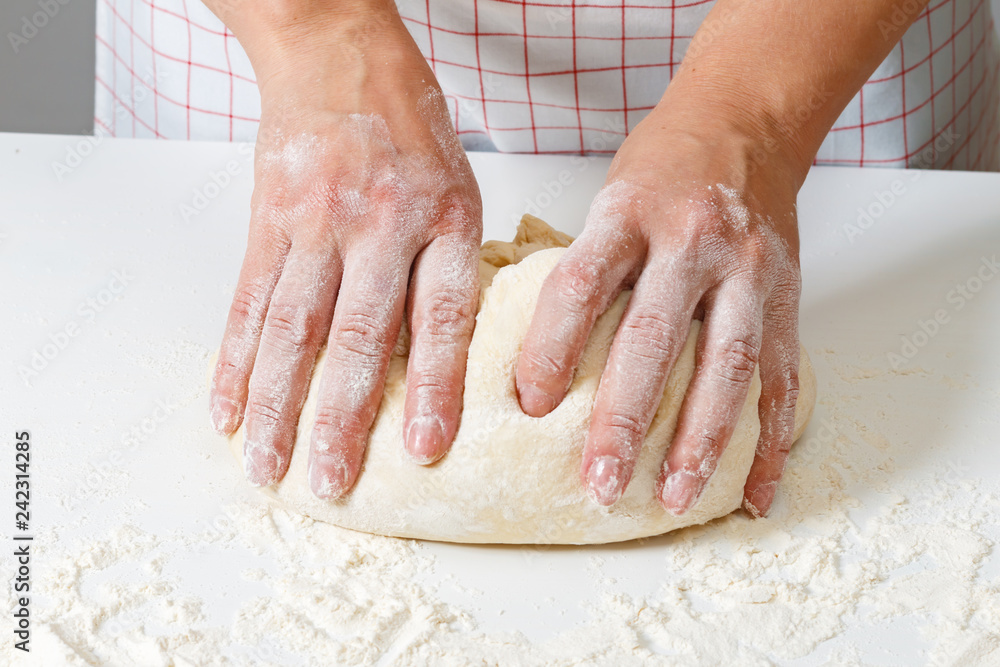Woman kneads raw fresh dough with hands on the table