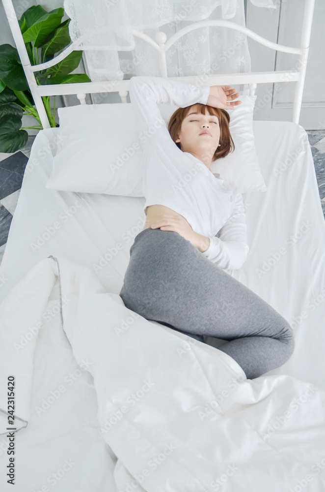 On the bed in the white room.Beautiful woman sleeping in the bedroom.Asian women sleep well.Hands on his forehead, women.Warm tone.