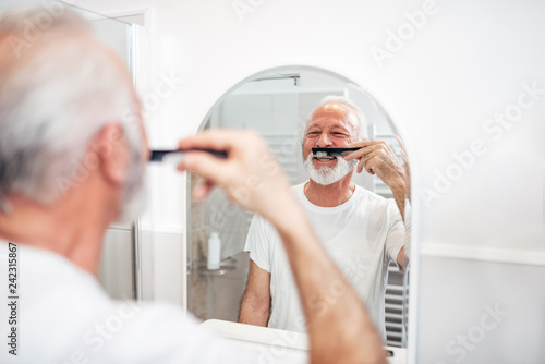 Smiling senior man combing his mustache in the bathroom.