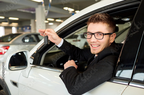 Man driver smiling holds car keys in car showroom
