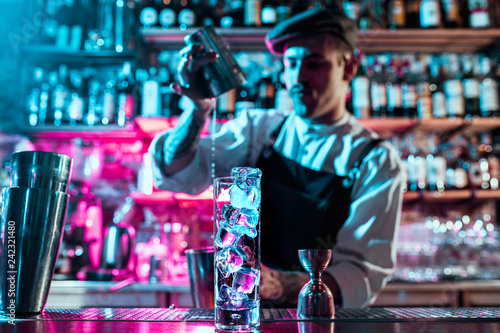 Expert barman is making cocktail at night club or bar. Glass of fiery cocktail on the bar counter against the background of bartenders hands with fire. Barman day concept photo