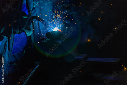 Welder in gloves welds a metal part in the factory. Glare of spark and smoke during the wizard