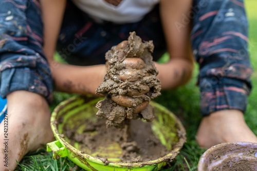 Closeup of toddler boy sitting barefoot in a green grass playing with mud