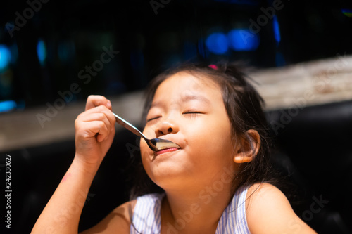 Happy asian child girl eating ice cream and she have spoon in her mouth in restaurant.Enjoying delicious face. 