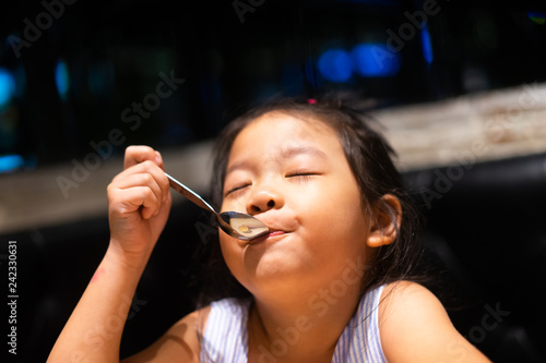 Happy asian child girl eating ice cream and she have spoon in her mouth in restaurant.Enjoying delicious face. 