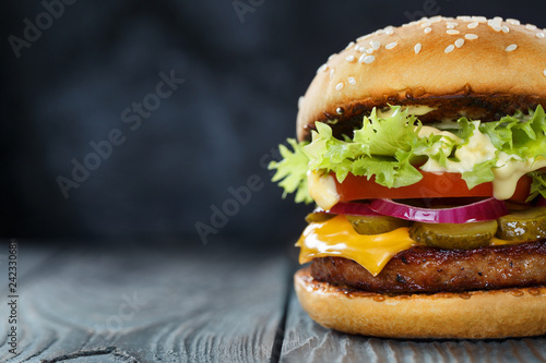 Close-up of delicious fresh home made burger with lettuce, cheese, onion and tomato on a dark background