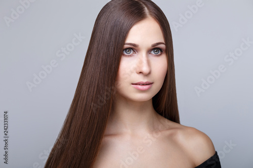 Beauty portrait. Young beautiful woman with straight brunette hair and clear healthy glowing skin at studio on grey background. Model girl with shiny smooth healthy hair. Skin and hair care products.