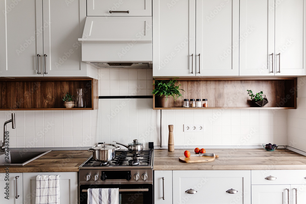 Fototapeta premium Cooking food on modern kitchen with furniture in grey color and wooden tabletop. Knife on wooden cutting board with vegetables, pepper, spices. Stylish kitchen interior in scandinavian style