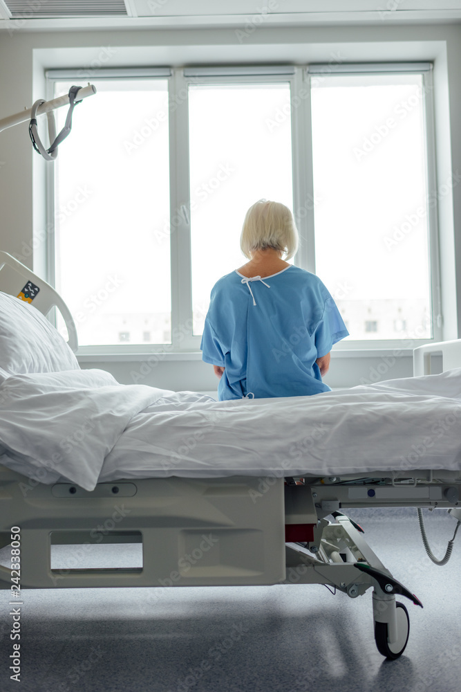 back view of lonely senior woman sitting on bed in hospital ward back view of lonely senior woman sitting on bed in hospital ward