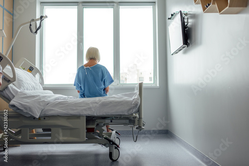Foto back view of lonely senior woman sitting on bed in hospital ward with copy space
