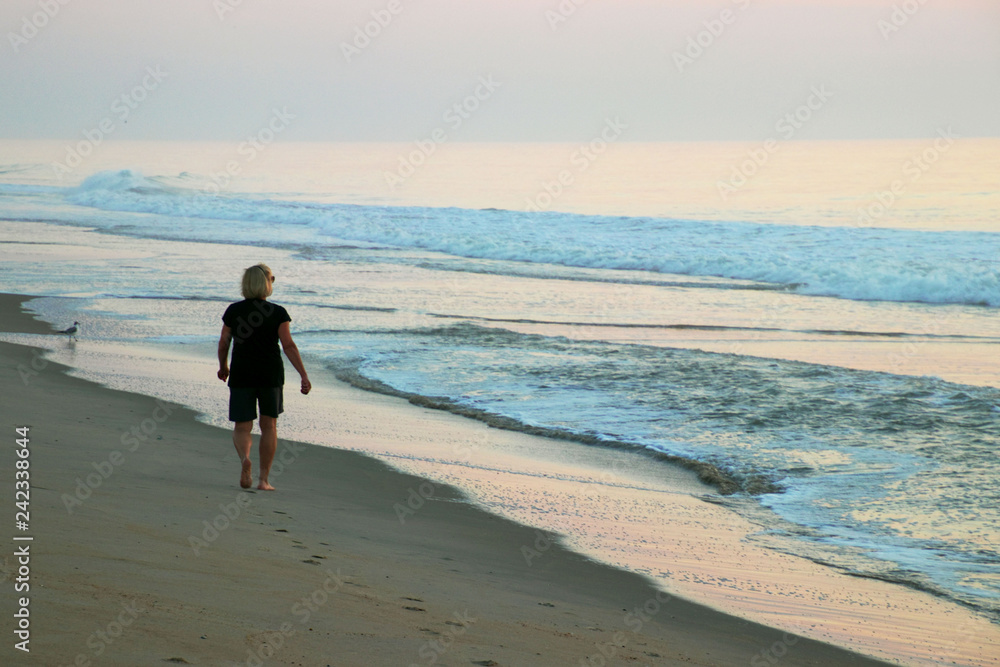 Woman walking on the beach at sunrise.