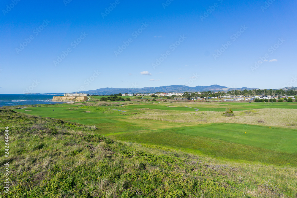 Golf course on the cliffs of the pacific ocean coast, resort and villas in the background, Half Moon Bay, California