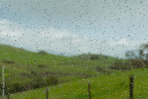 Drops of rain on the window; blurred green meadows in the background; shallow depth of field