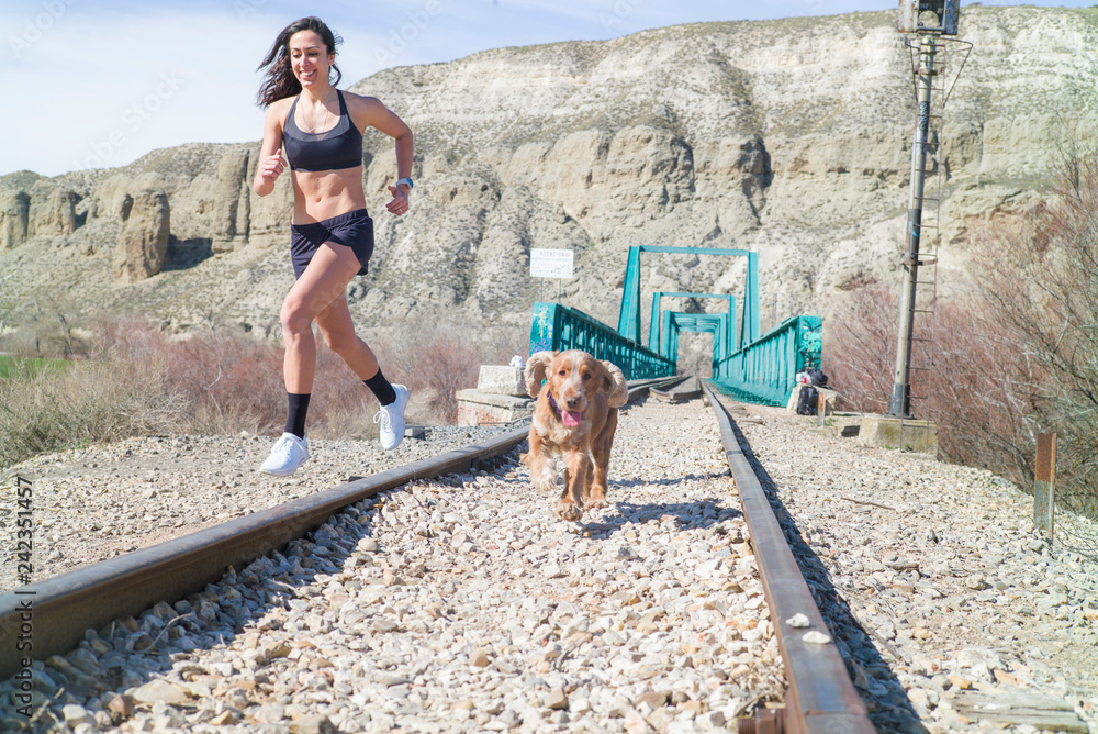 Young woman running through the railroad with dog Young woman running through the railroad with dog
