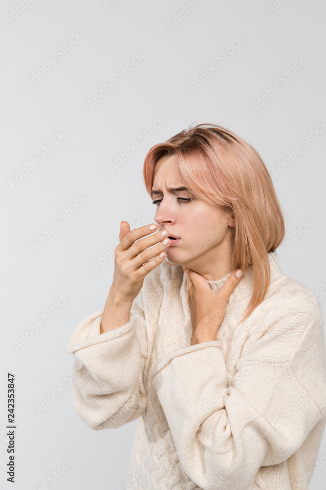 Vertical studio portrait of young unhealthy coughing blonde woman in warm sweater/suffers from cold and flu, coughing a lot, sore throat, feeling sick, chest pain, medicine and healthcare concept. Vertical studio portrait of young unhealthy coughing blonde woman in warm sweater/suffers from cold and flu, coughing a lot, sore throat, feeling sick, chest pain, medicine and healthcare concept.