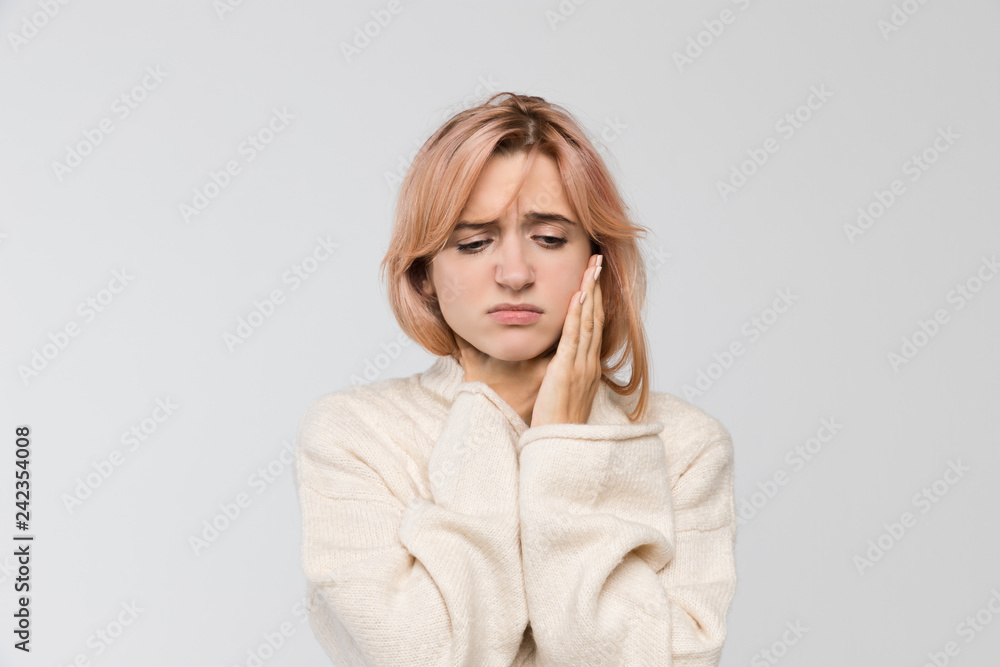 Close-up studio portrait of young blonde woman in warm sweater suffering from severe toothache, holding her cheek, feeling pain, tooth pain and dentistry, teeth problem, dental and healthcare concept. Close-up studio portrait of young blonde woman in warm sweater suffering from severe toothache, holding her cheek, feeling pain, tooth pain and dentistry, teeth problem, dental and healthcare concept.