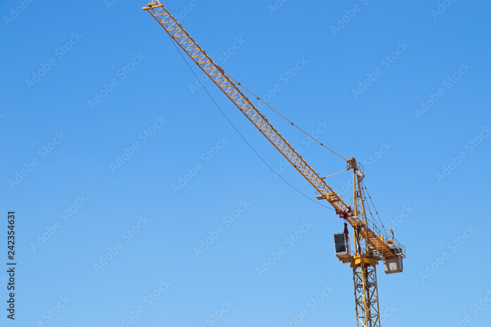 A yellow construction crane isolated on a blue sky background. Building and engineering concept image. A yellow construction crane isolated on a blue sky background. Building and engineering concept image.