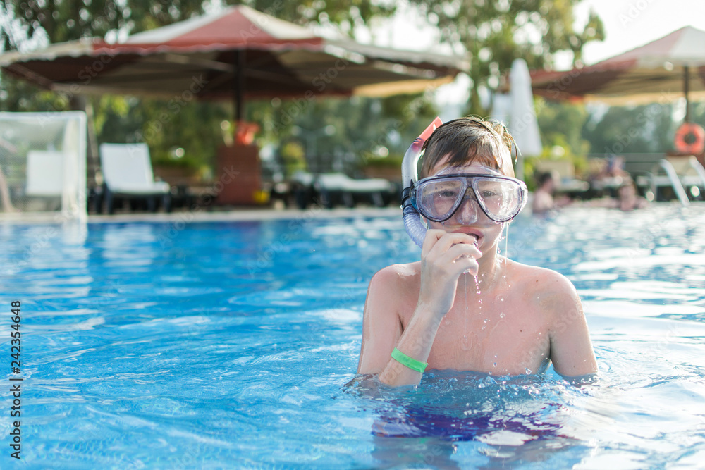 Teenager boy wearing mask swimming in the pool. Happy holiday concept. Cute happy little boy swimming and snorking in the swimming pool.