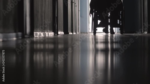 Low section of silhouette of nurse pushing paraplegic man on wheelchair along hospital hallway