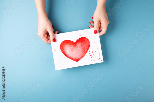 Female hands holding card with heart on blue background.