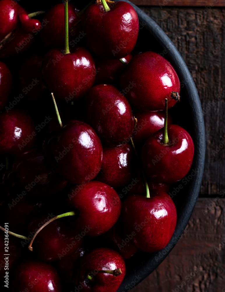 Top view of cherries in a black bowl over a wood table Top view of cherries in a black bowl over a wood table