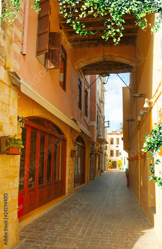 Romantic old buildings and cobblestone streets of Crete island, Greece. Bright sunny day. Green climbing plants.