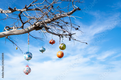 Tree decorated with Christmas ornaments over clear blue sky