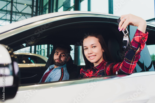 Photo of young smiling mixed race woman sitting inside her new car and holding key. Concept for car rental.