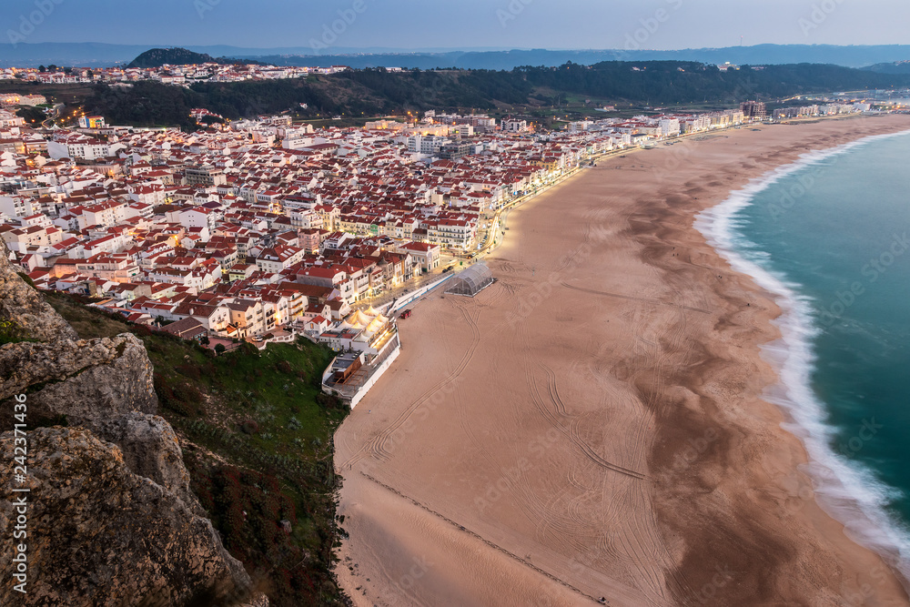 Nazaré beach, in Portugal, at dusk with lights on, seen from the SÃ­tio's viewpoint.