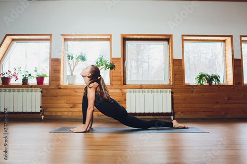 Attractive happy young woman working out indoors. Beautiful model doing exercises on blue mat. Standing in low lunge exercise horse rider or ashwa sanchalasana pose . Full length. Side view. photo