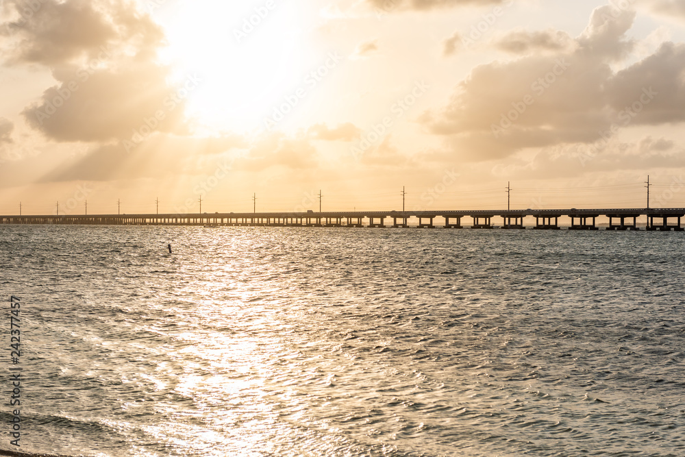 Seven Mile Bridge landscape of Florida Keys reflection of sun on water atlantic ocean and Overseas Highway road with horizon clouds sunset rays