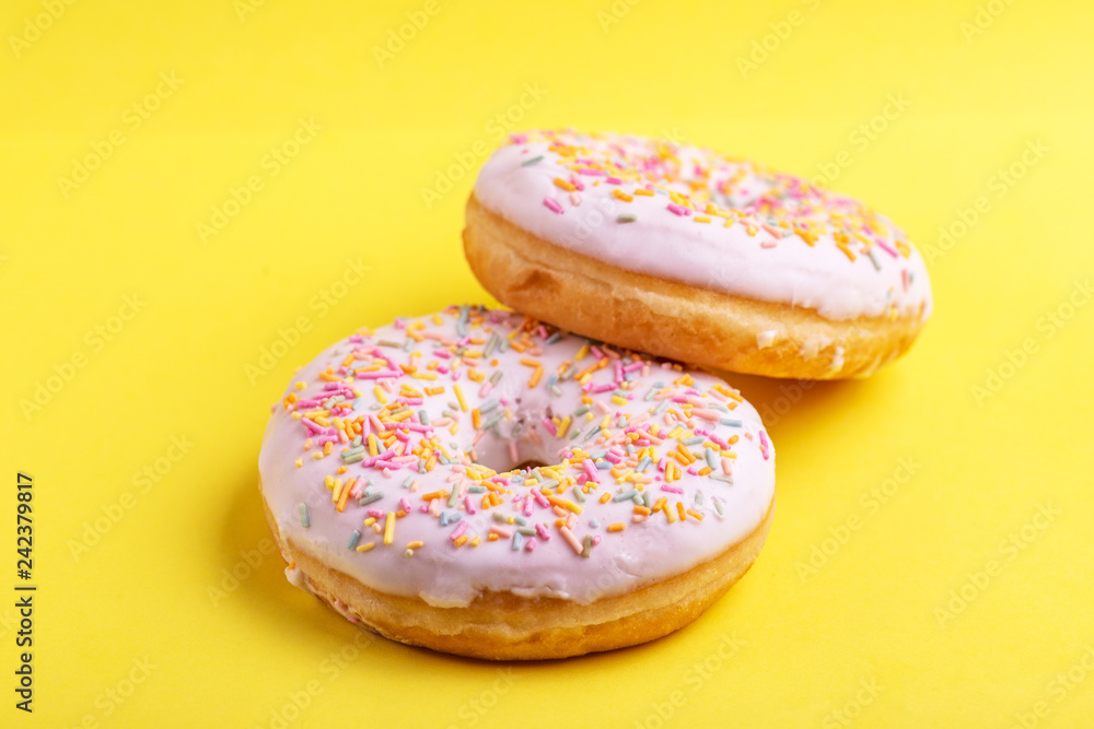 Two delicious vanilla donuts with sprinkle on bright yellow background Two delicious vanilla donuts with sprinkle on bright yellow background