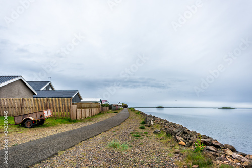 Landscape view of village by fjord water river in fishing town called Hofn in Iceland with houses wooden fence and trail path