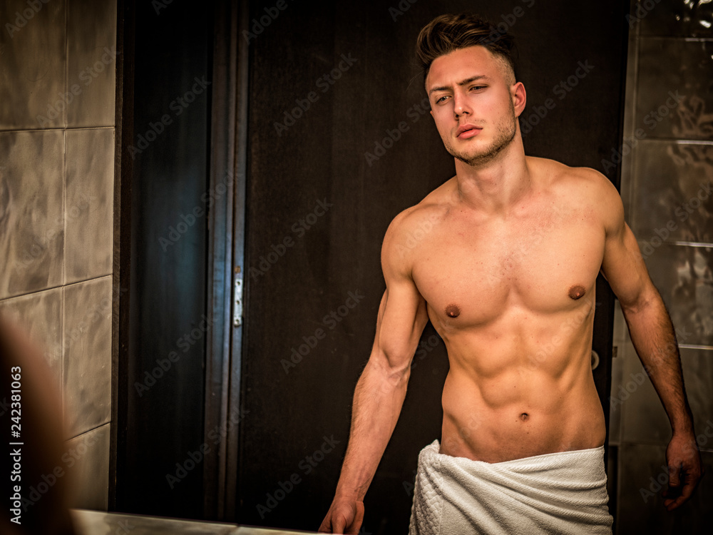 Shirtless handsome young man looking at himself in bathroom mirror in the morning Shirtless handsome young man looking at himself in bathroom mirror in the morning