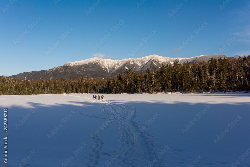 a group of hikers walk across a frozen lake with the White Moutains of New Hampshire in the background a group of hikers walk across a frozen lake with the White Moutains of New Hampshire in the background
