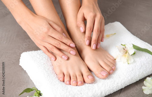 Fototapeta Naklejka Na Ścianę i Meble -  Woman touching her smooth feet, towel and flowers on grey background, closeup. Spa treatment
