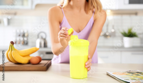 Young woman opening bottle of protein shake at table with ingredients, closeup