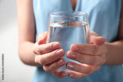 Woman holding glass with fresh water against light background, closeup