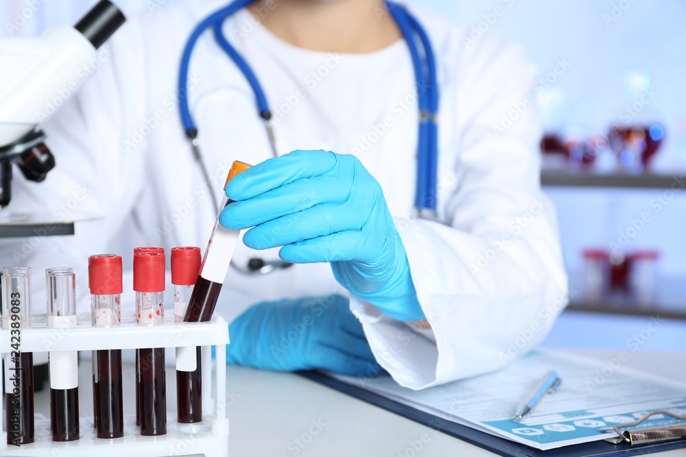 Laboratory worker taking test tube with blood sample from rack for analysis on table Laboratory worker taking test tube with blood sample from rack for analysis on table