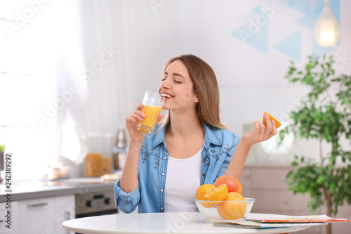Beautiful young woman drinking fresh orange juice in kitchen. Healthy diet