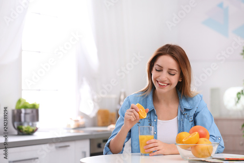 Happy young woman squeezing orange juice into glass at table in kitchen, space for text. Healthy diet
