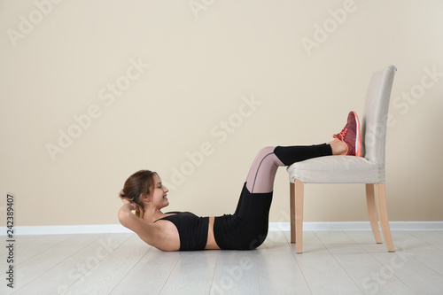 Young woman exercising with chair near color wall. Home fitness